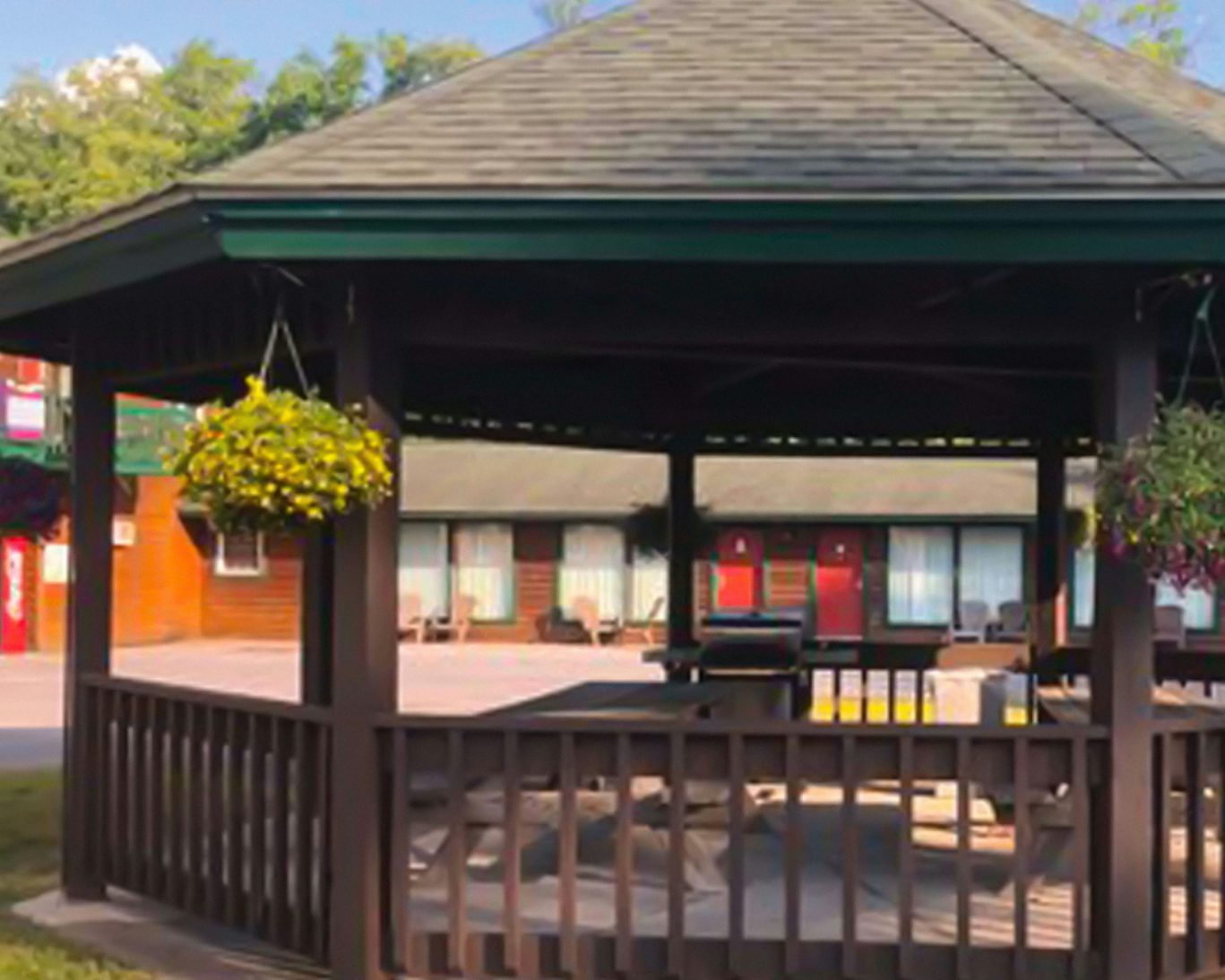 Wooden gazebo with hanging flower baskets and picnic tables at hotel courtyard.