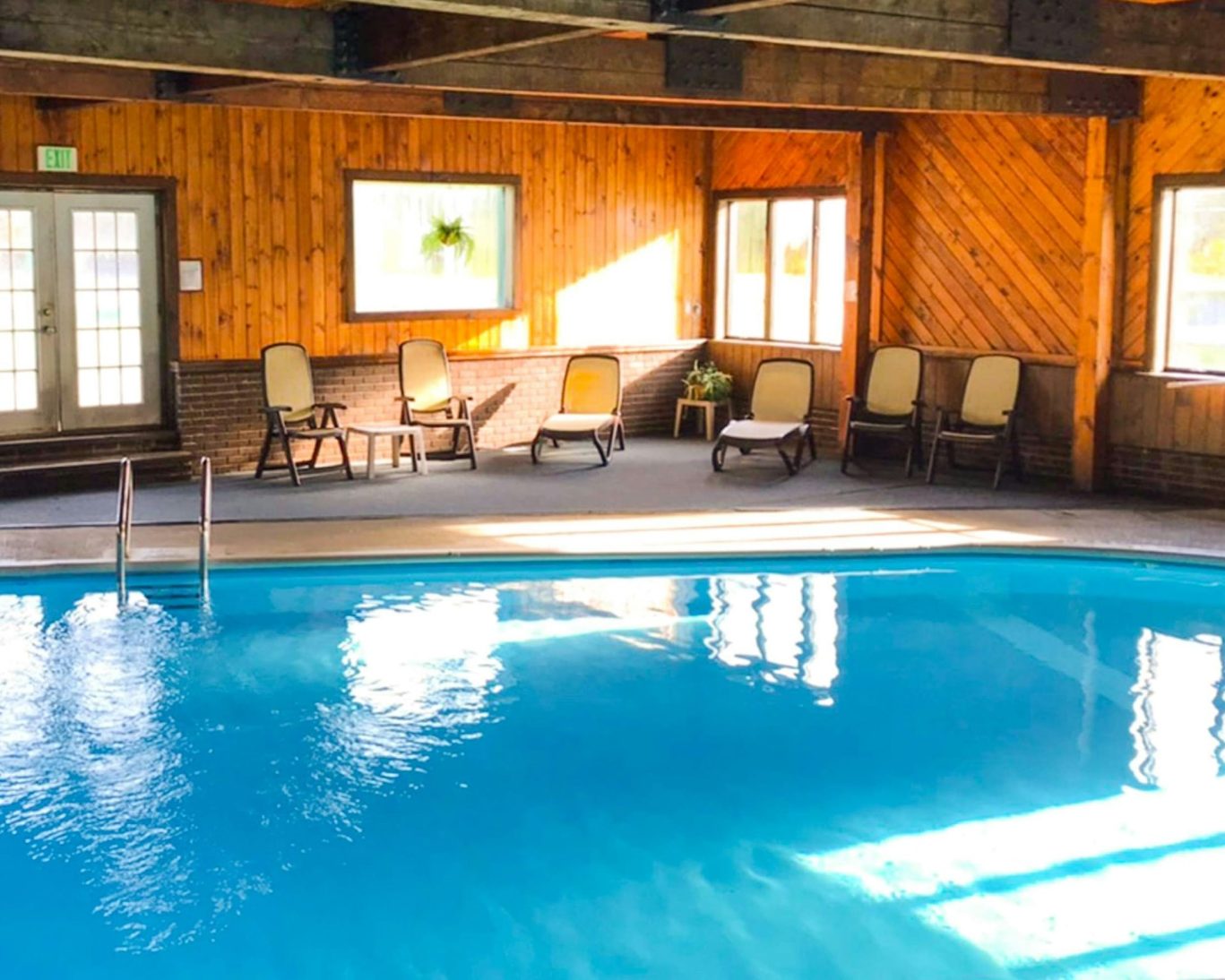 Bright indoor swimming pool area with lounge chairs at a rustic-style hotel.