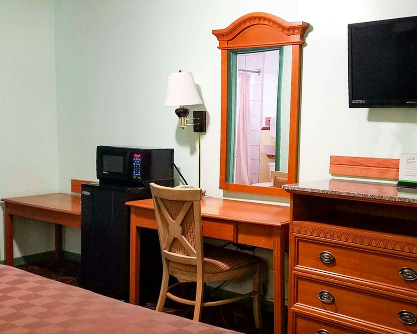 Guest room at American Inn & Suites with microwave, mini fridge, desk, and mirror.