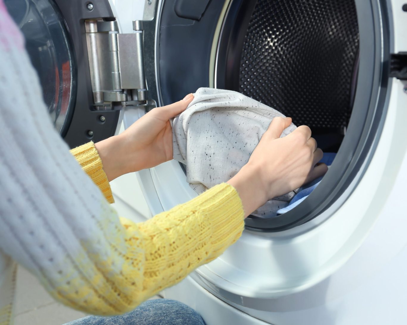 Guest loading clothes into front-load washing machine at hotel laundry facility.