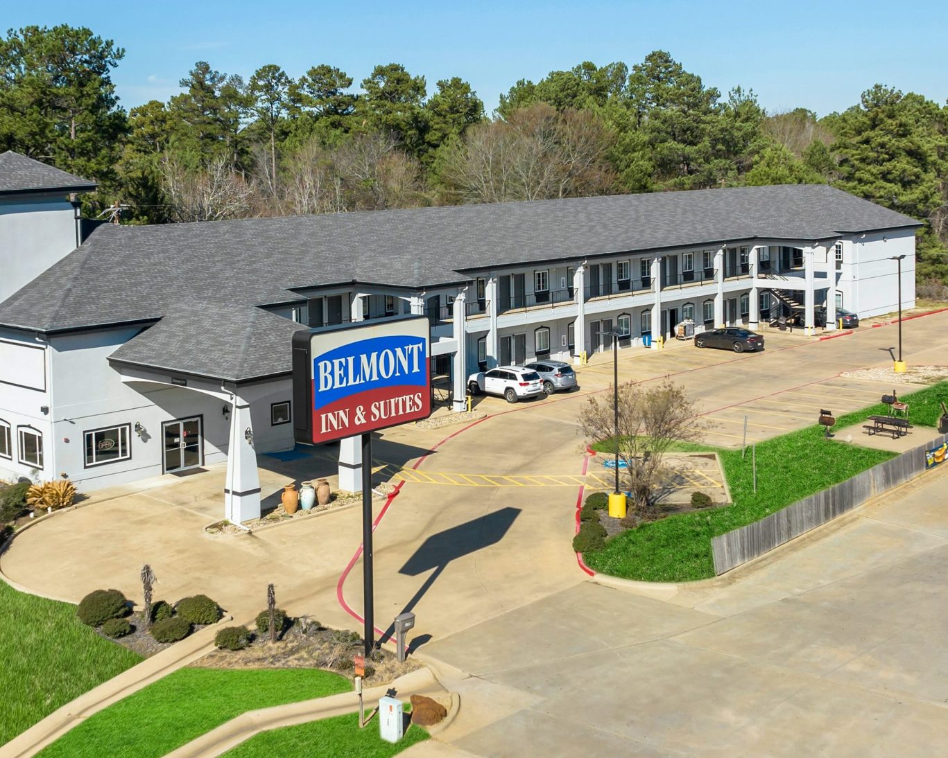 Belmont Inn & Suites exterior with parking lot and hotel sign surrounded by trees.