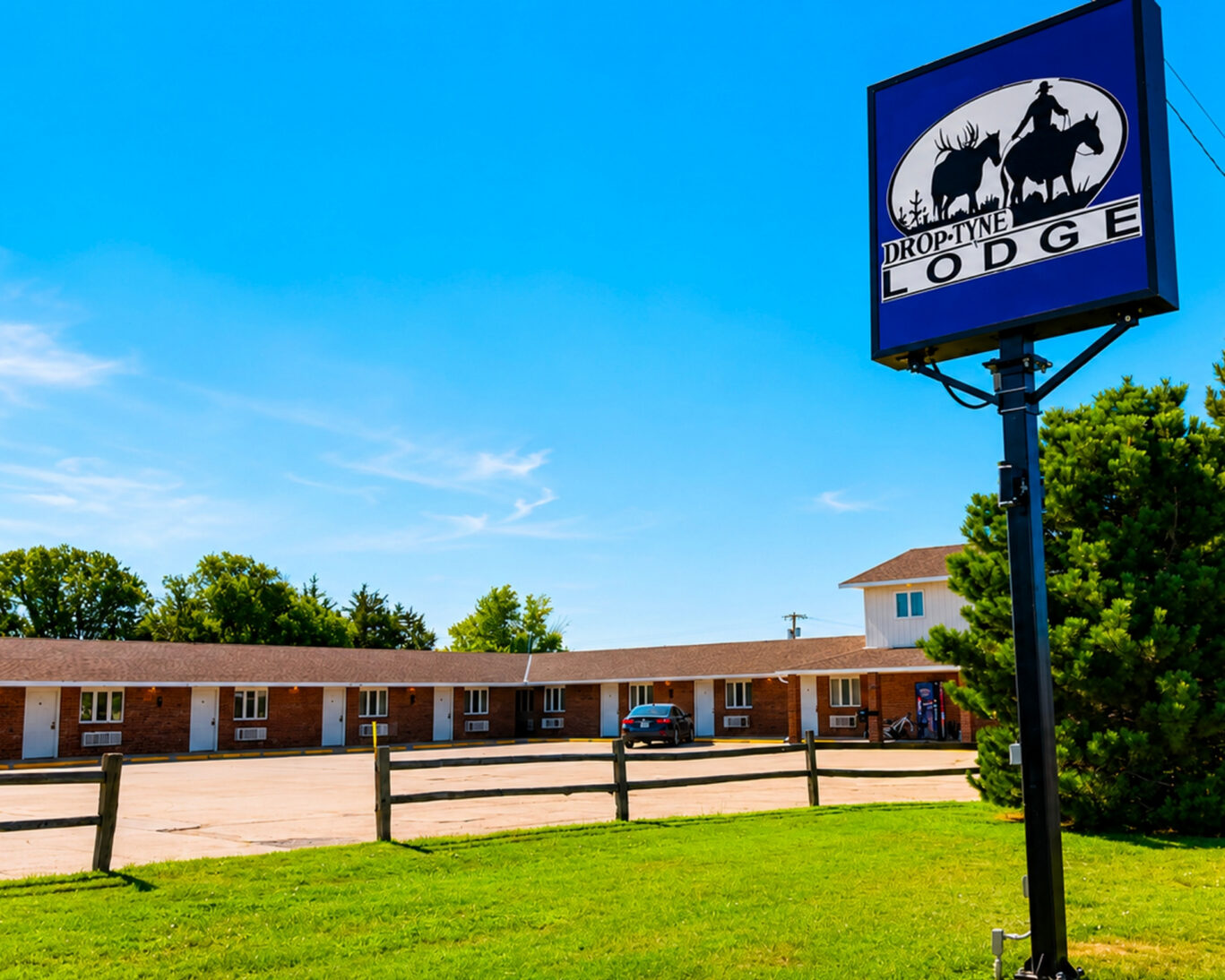 Illuminated roadside sign at Drop-Tyne Lodge with single-story brick guest room wing and parking lot behind.