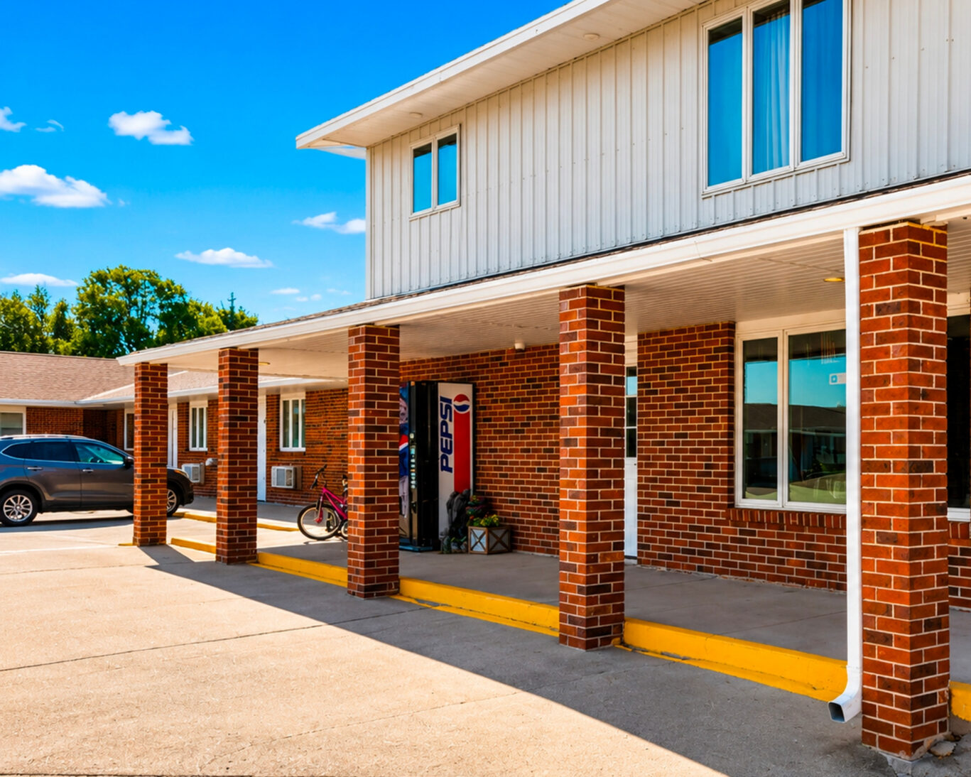 Covered entrance walkway at Drop-Tyne Lodge with brick columns, vending machine, and adjacent guest parking.
