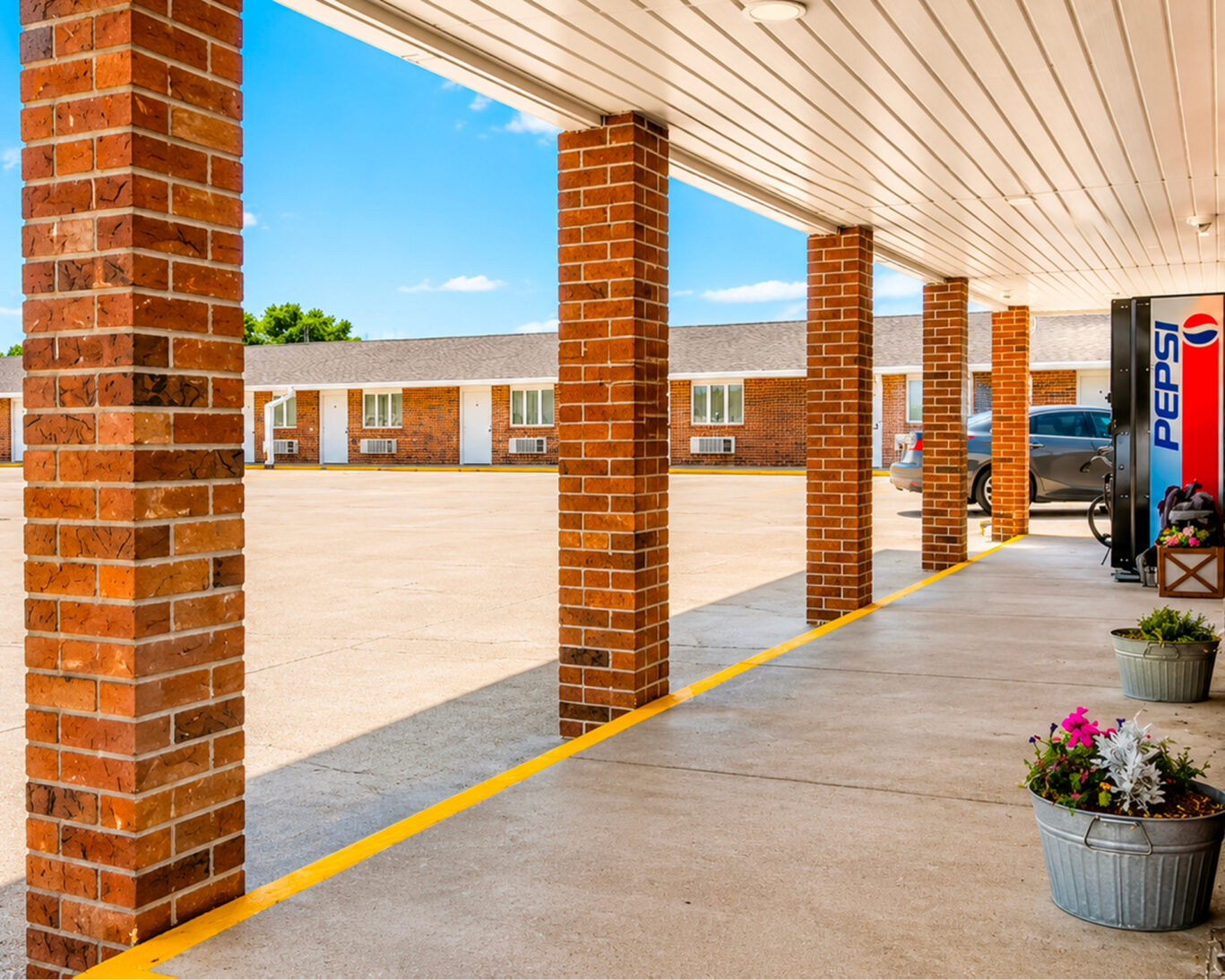 Covered walkway at Drop-Tyne Lodge looking across the parking lot toward ground-floor guest room entrances.
