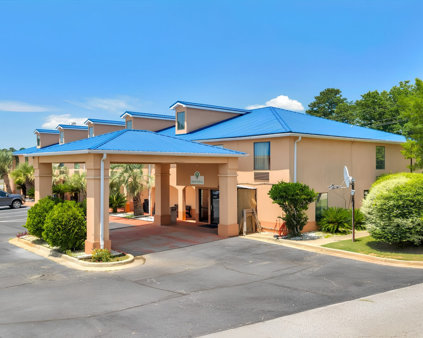 Exterior view of Gray Inn and Suites showing the covered entrance with columns, blue metal roof, and landscaped shrubs.