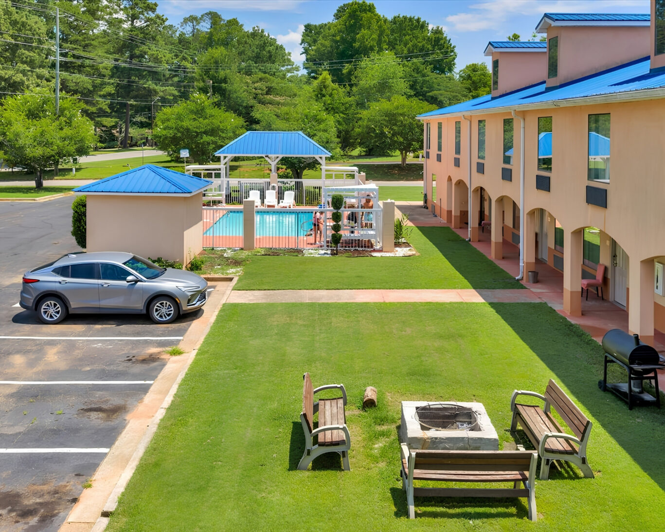 Courtyard view of Gray Inn and Suites with fenced outdoor pool, gazebo, fire pit with benches, and barbecue grill on the lawn.