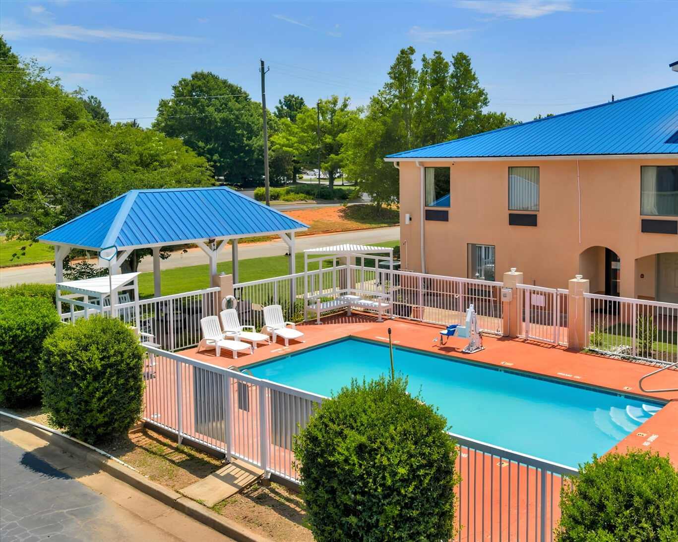 Courtyard view of Gray Inn and Suites with fenced outdoor pool, gazebo, fire pit with benches, and barbecue grill on the lawn.