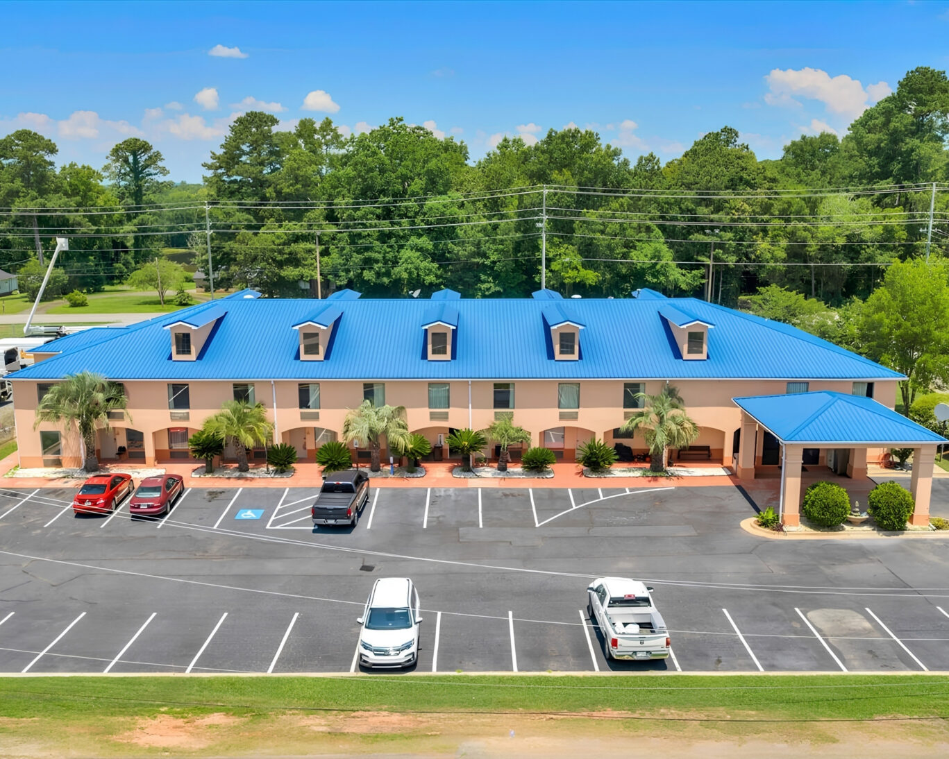 Aerial view of Gray Inn and Suites showing the full two-story building with blue roof, dormer windows, palm landscaping, and guest parking lot.