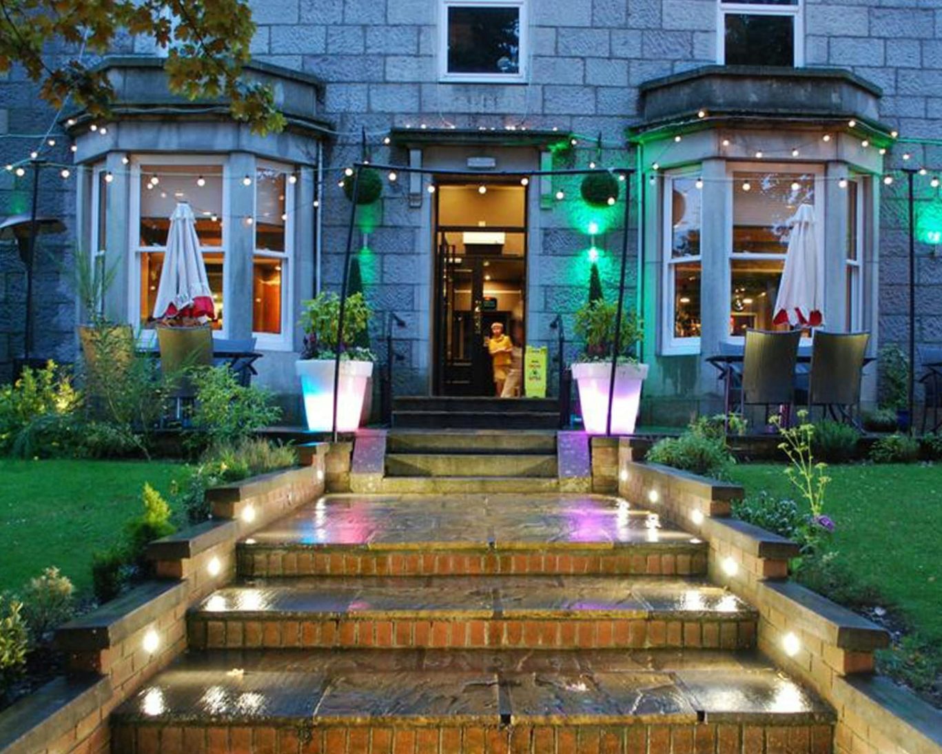 Front exterior of Great Western Hotel with illuminated garden steps and outdoor seating.