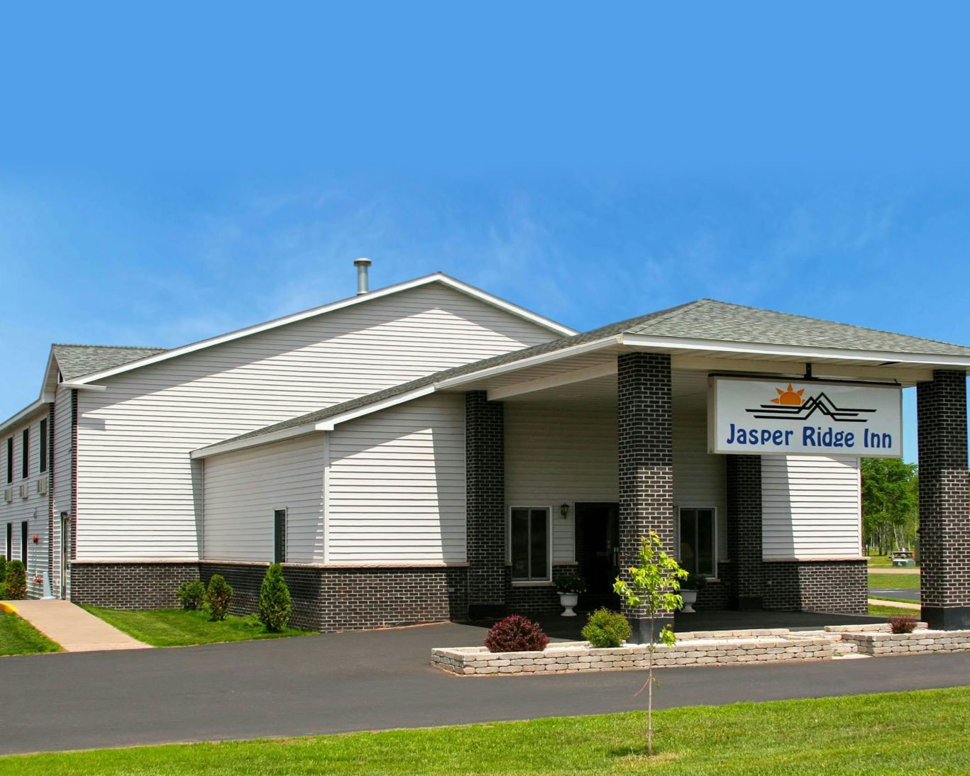 Exterior view of Jasper Ridge Inn in Ishpeming, Michigan, with white siding and covered entrance under a blue sky.
