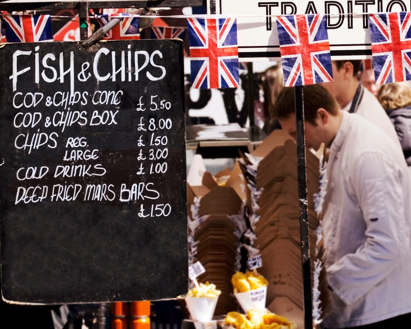 Traditional British fish and chips street food stall with Union Jack flags in London market.