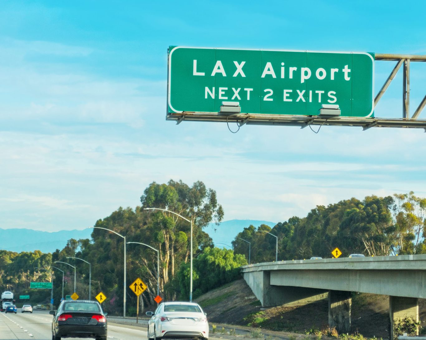 Highway exit sign for LAX Airport in Los Angeles with traffic on a clear day.
