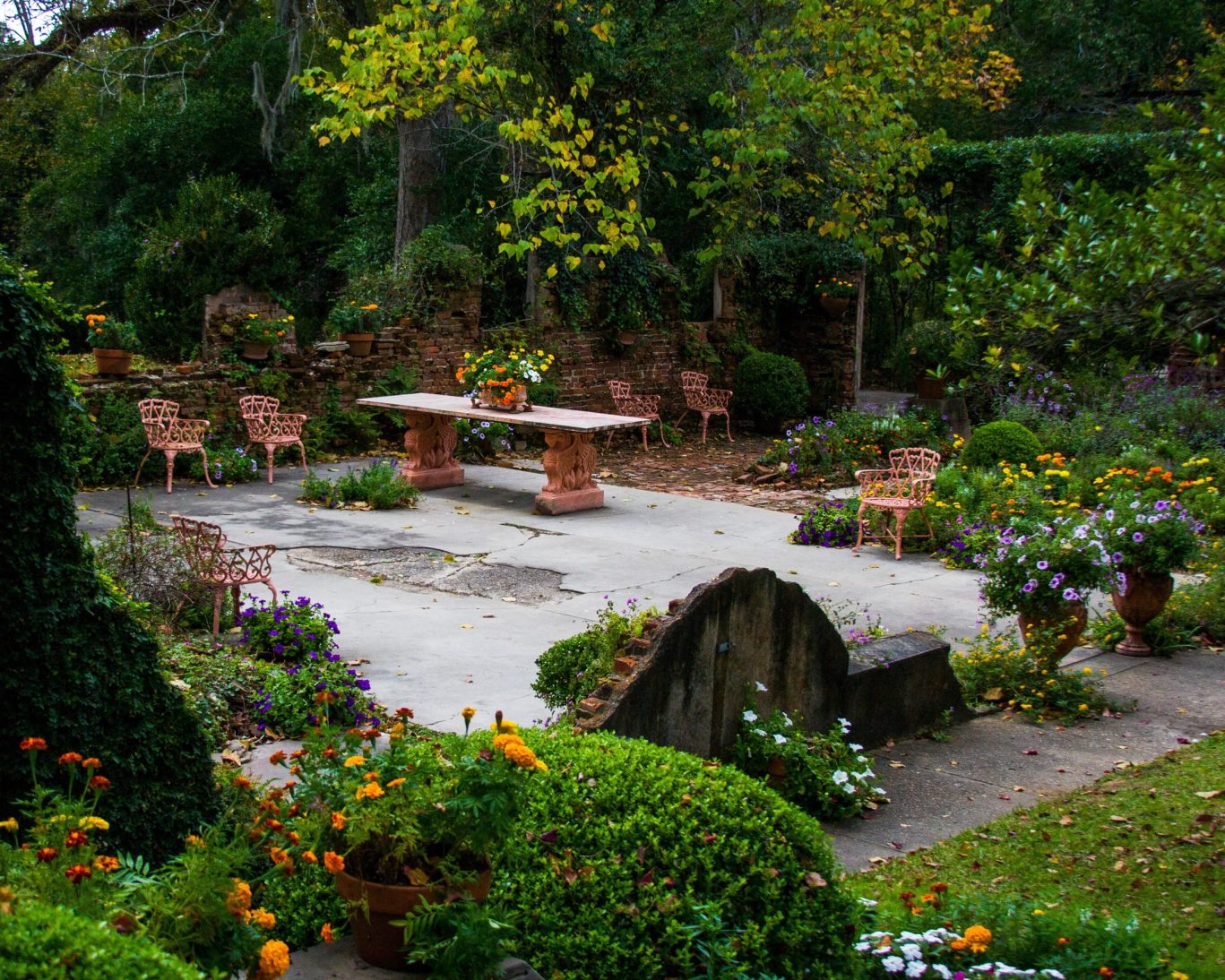 Historic Afton Villa Gardens featuring elegant stone patio, wrought iron chairs, and vibrant seasonal flowers in St. Francisville, Louisiana.