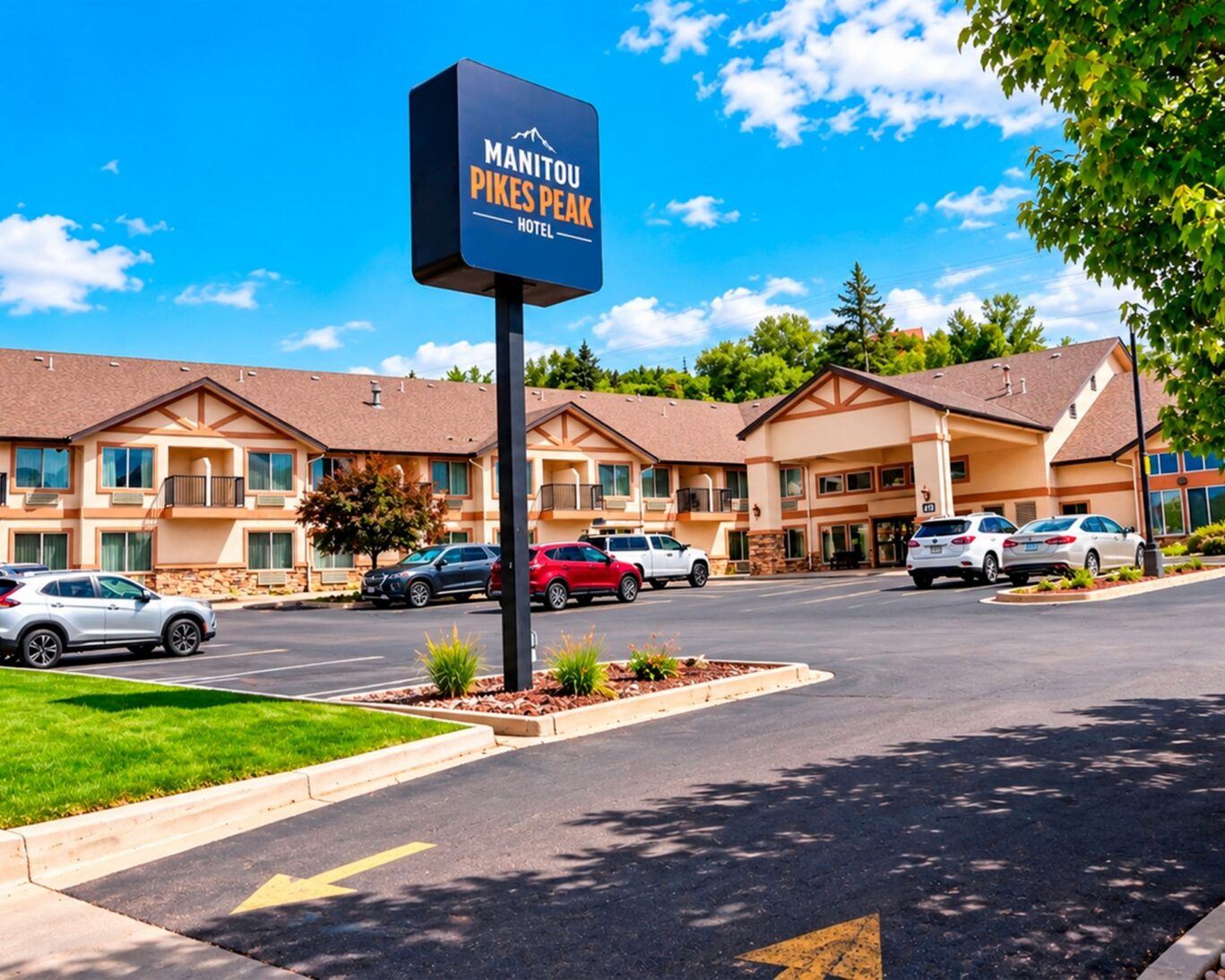 Exterior of Manitou Pikes Peak Hotel showing the property sign, two-story building, and guest parking lot.