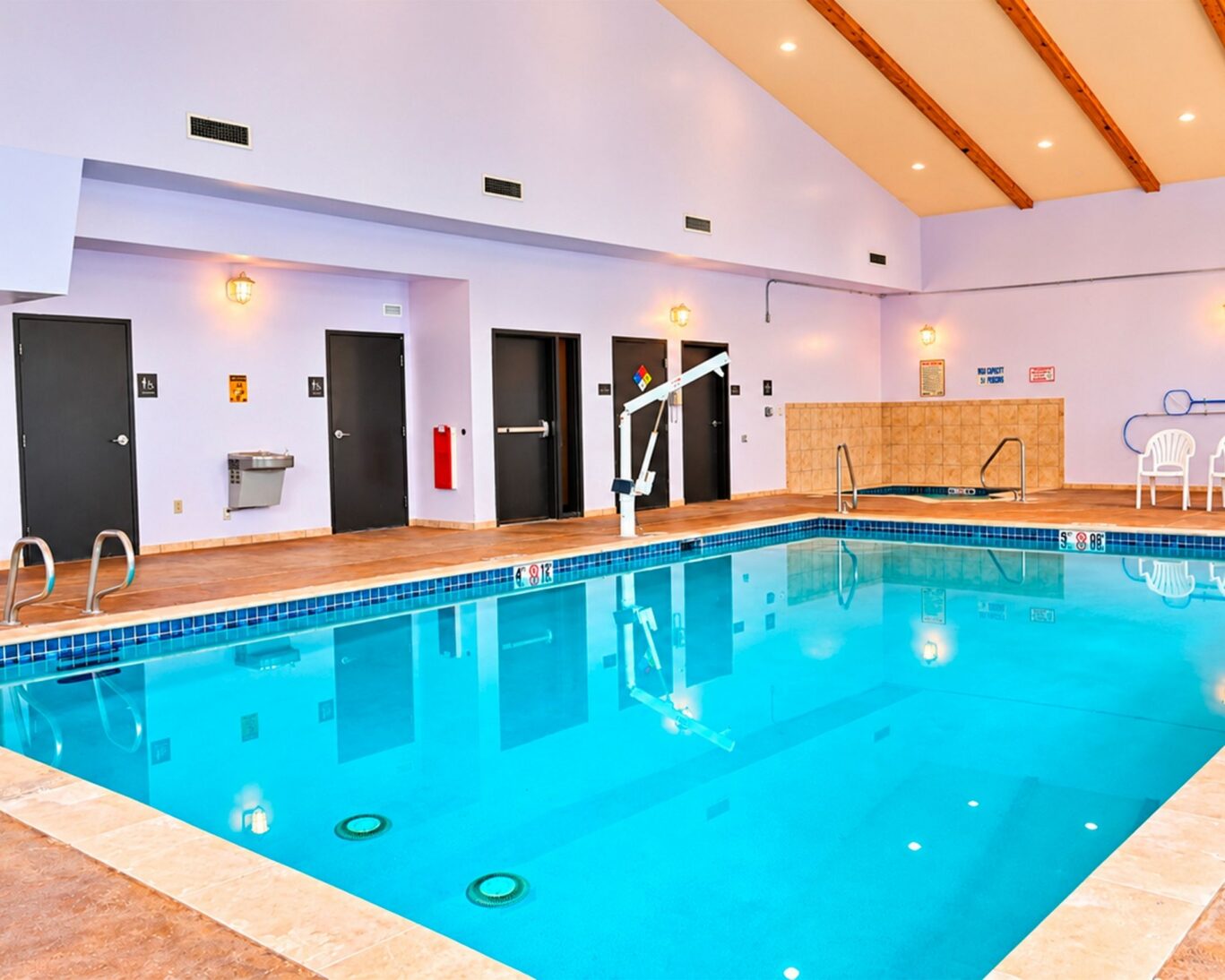 Indoor pool at Manitou Pikes Peak Hotel with an accessible pool lift, handrails, hot tub, and poolside chairs.