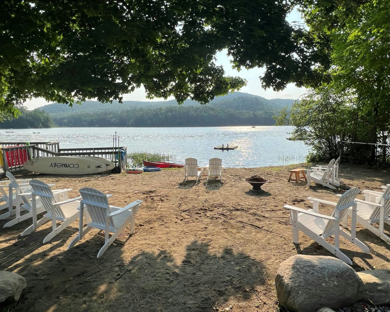 Lakeside beach with Adirondack chairs and paddleboards at Lake Luzerne Motel, New York.