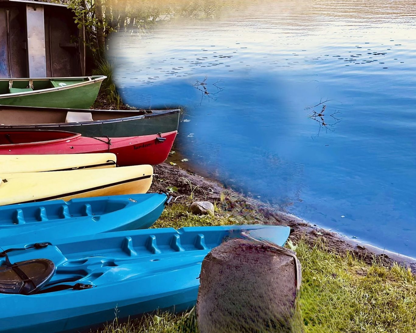 Colorful kayaks and canoes lined up on grassy lake shore at Lake Luzerne Motel.