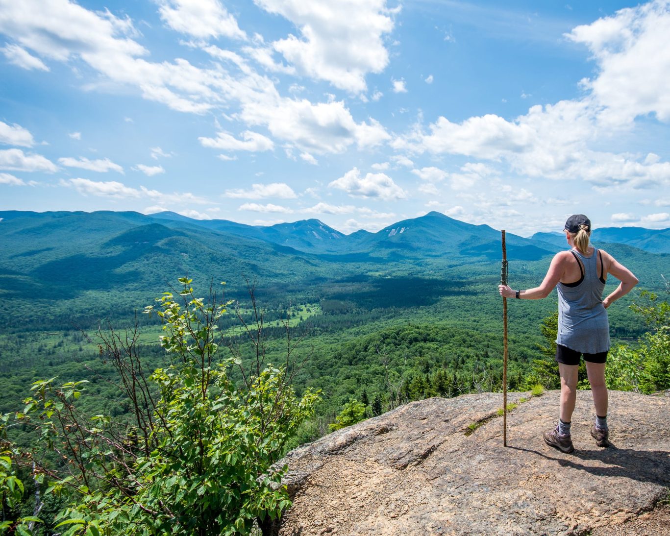 Woman hiking scenic Adirondack Mountains trail with panoramic forest views.