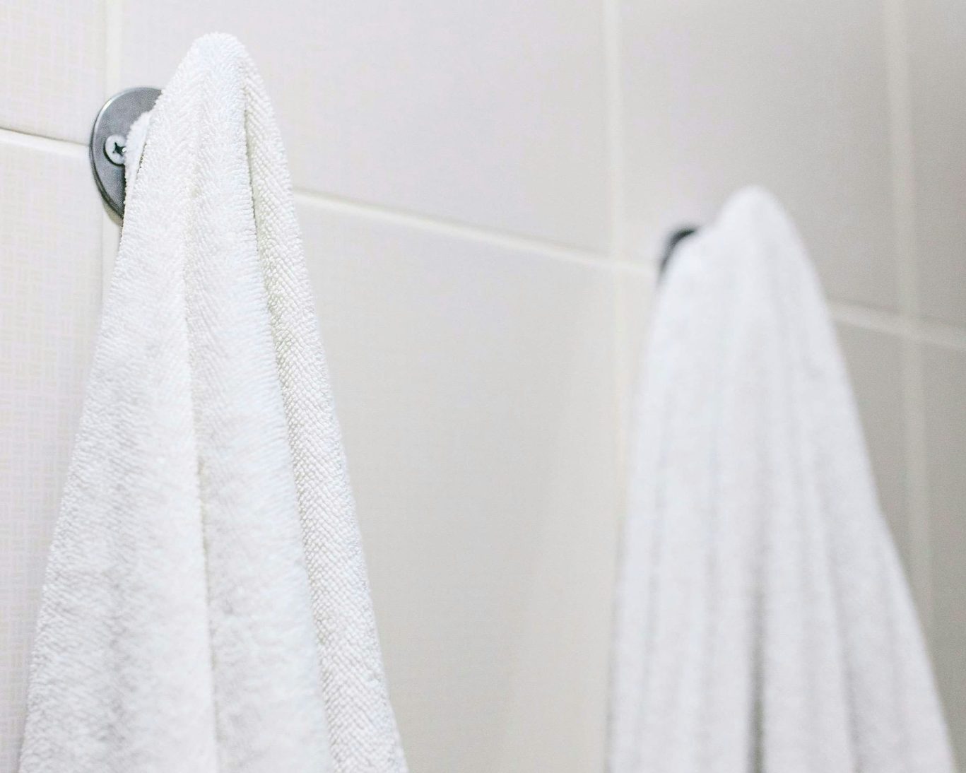 Clean white towels hanging on wall hooks in guest bathroom at Santa Cruz Inn Riverside.