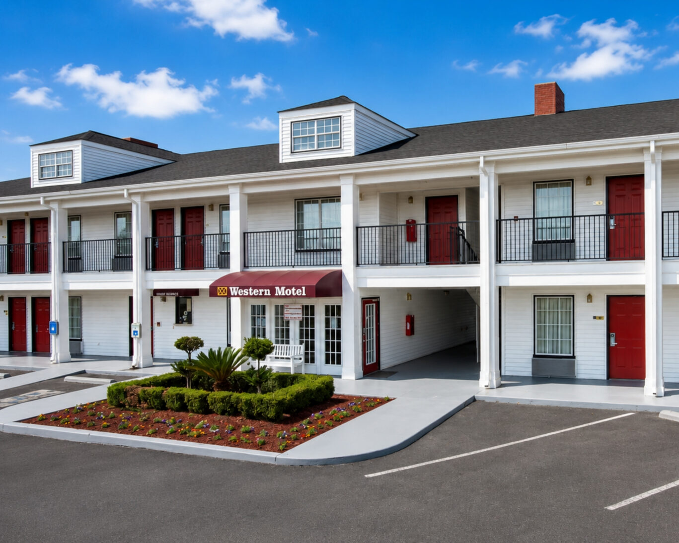 Two-story exterior of Western Motel with covered walkways, red guest room doors, and landscaped entrance beds.