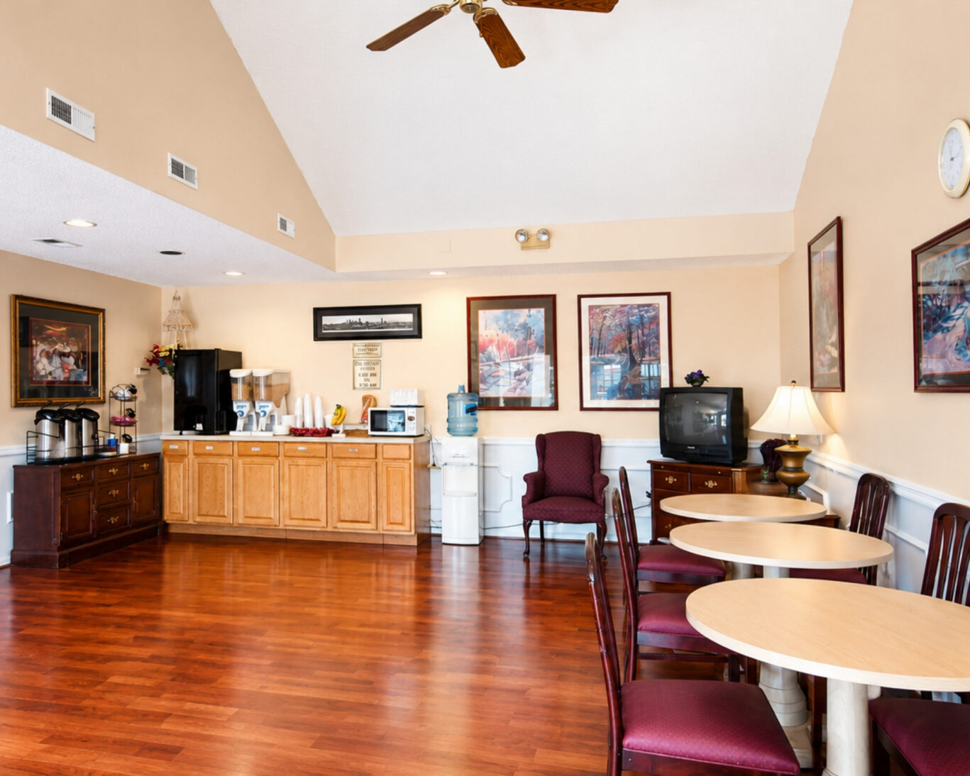 Seating area at Western Motel with round tables, coffee station, cereal dispensers, microwave, and hardwood floors.