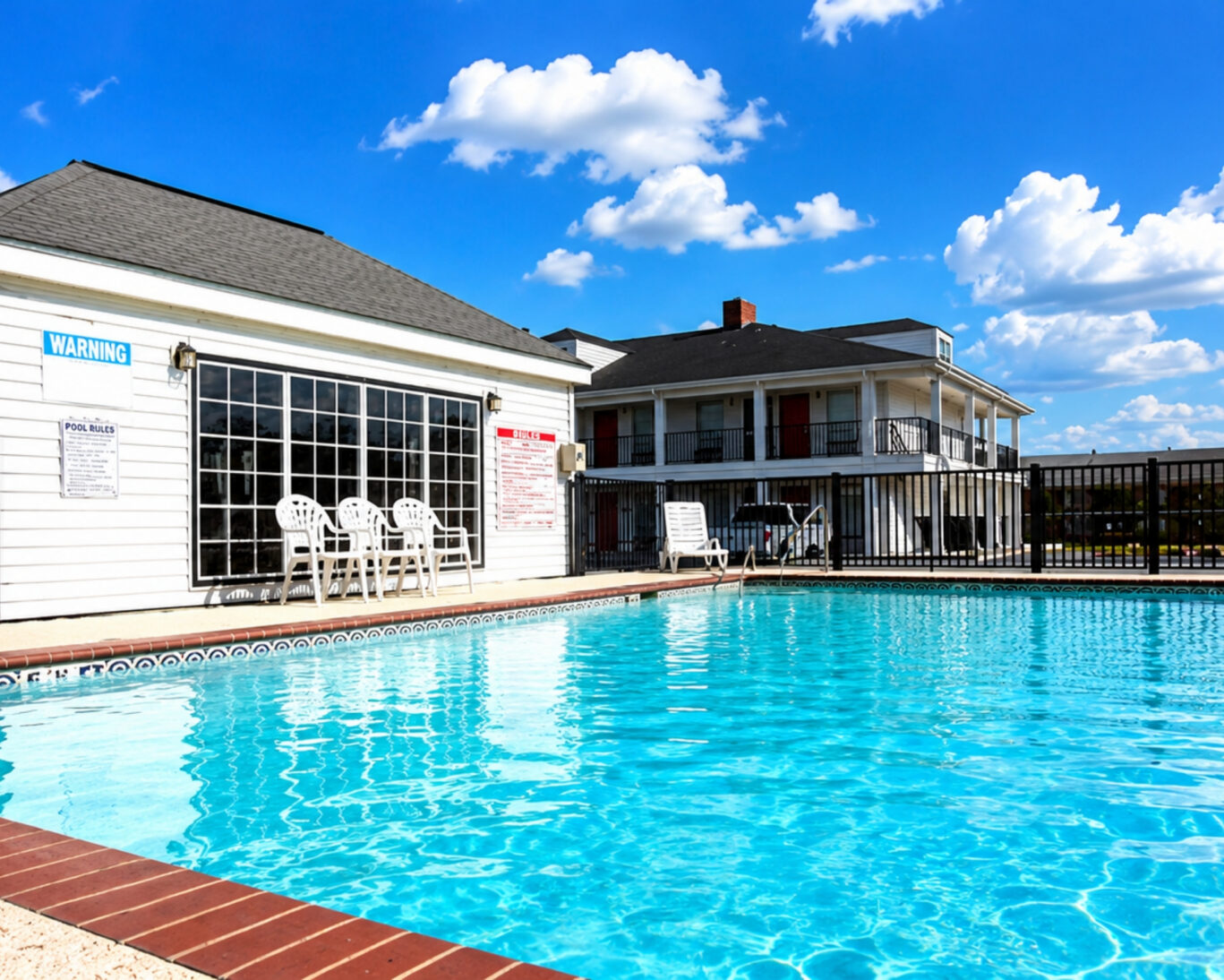 Fenced outdoor pool at Western Motel with patio chairs, pool rules signage, and guest rooms behind.