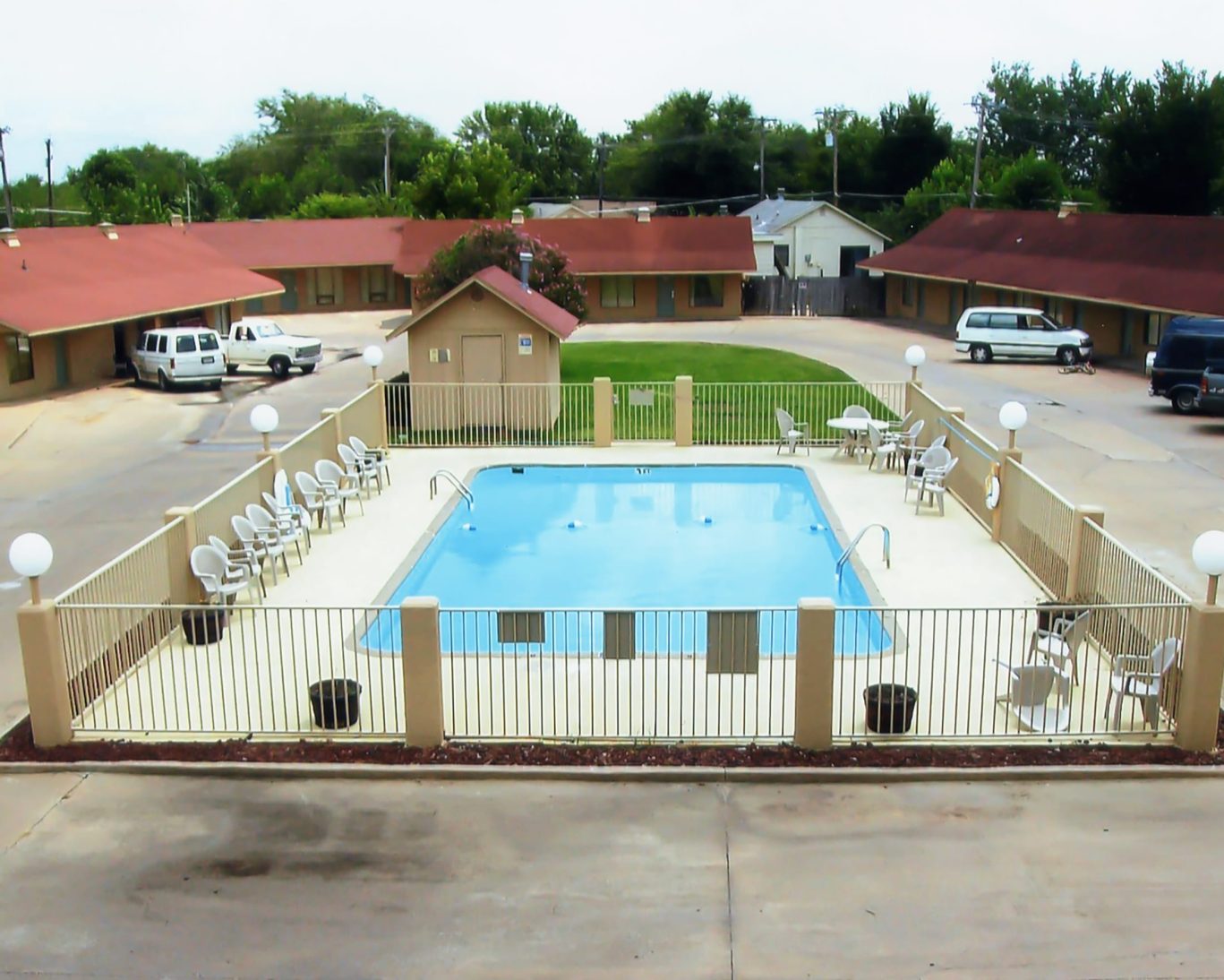 Fenced outdoor swimming pool area with lounge chairs at Will Rogers Inn.
