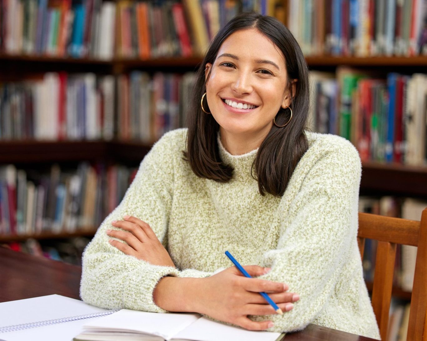 Smiling student studying with notebook and pen at university library desk.