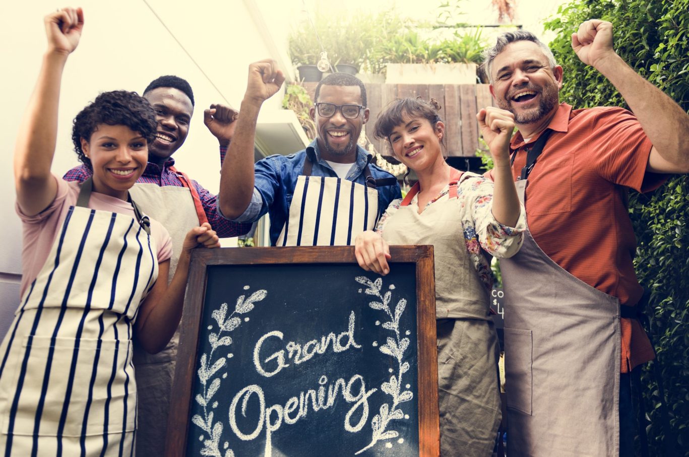 Excited group of entrepreneurs celebrating grand opening with handmade sign.