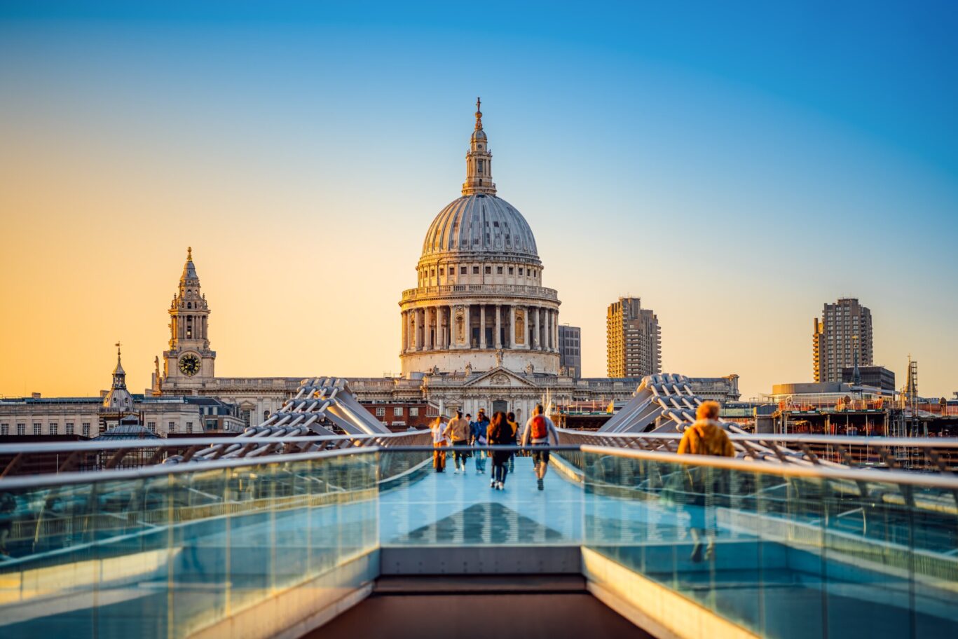 Tourists crossing the Millennium Bridge toward St. Paul’s Cathedral at sunset in central London, UK.