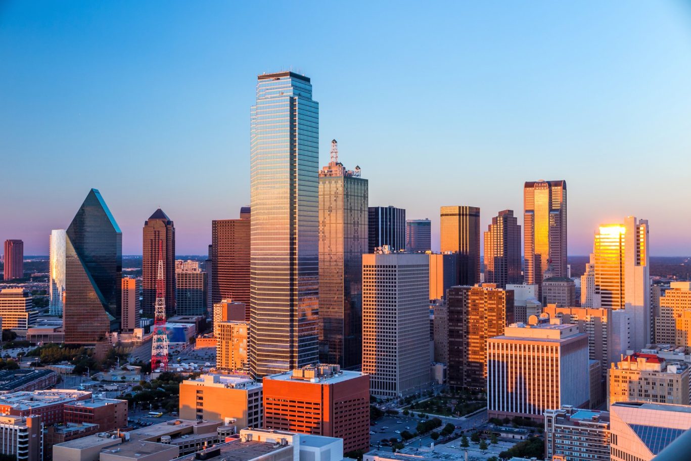 Downtown Dallas skyline at golden hour with high-rise buildings reflecting the sunset.