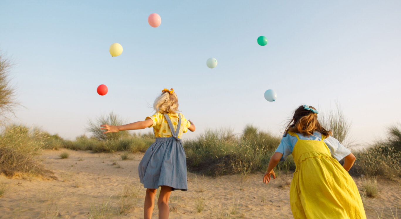 young girls running outside with multicoloured balloons in summer dresses