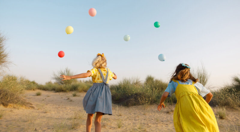 young girls running outside with multicoloured balloons in summer dresses
