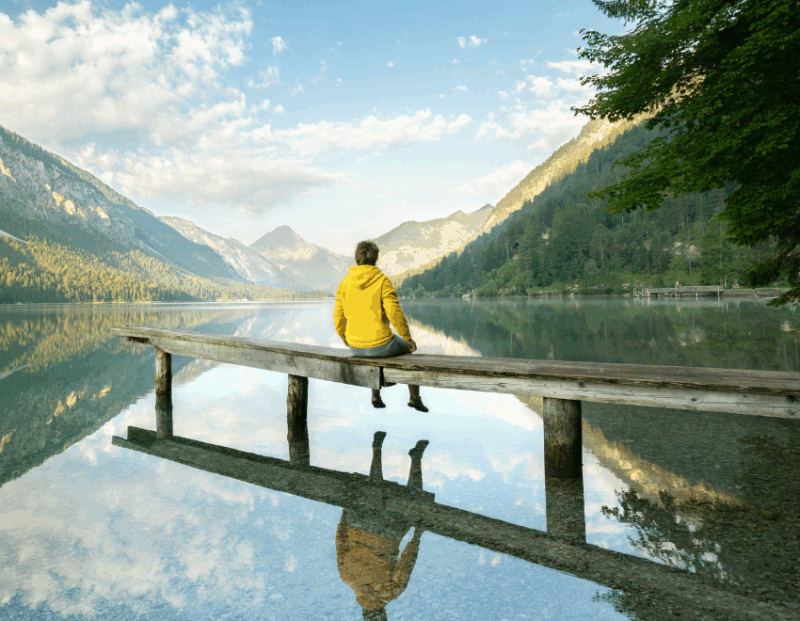 yellow coat man sitting looking out at a scenic lake